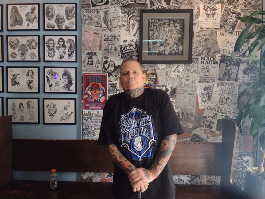 A+portrait+of+Jason+Brown%2C+owner+of+S.T.+Tattoo+and+lead+singer+for+Cycotic+Youth%2C+standing+in+front+of+tattoo+designs+and+art