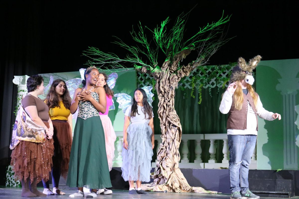In love with a donkey: Transformed Bottom (junior Willow Coder) accepts his new physical appearance as a group of fairies (freshmen Fae Livingstone, Daphne Rottenberg, Abisola Forrestor, Sage Smith, and Sofia Jimenez) look onward.