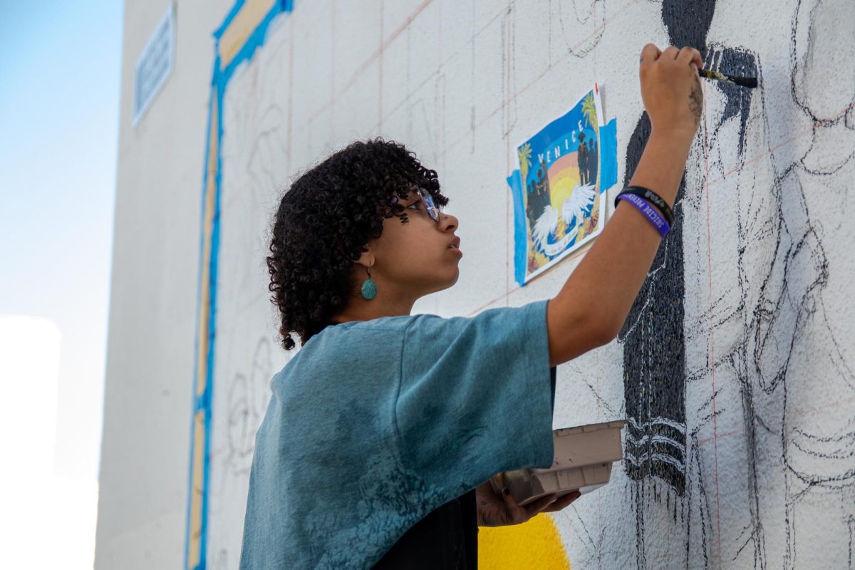 Vision of the future: Senior Jeannie Fischer helps paint a new mural between the West and Main Buildings during the final days before graduation. The mural is a collaboration between Venice's M.E.Ch.A chapter and Art Factory, a club dedicated to art-making. The mural centers on silhouettes with traditional Latin American clothing and a backdrop of a sunset on Venice Beach---adorned with palm trees, cempasúchil (also known as marigolds), and monarch butterflies.