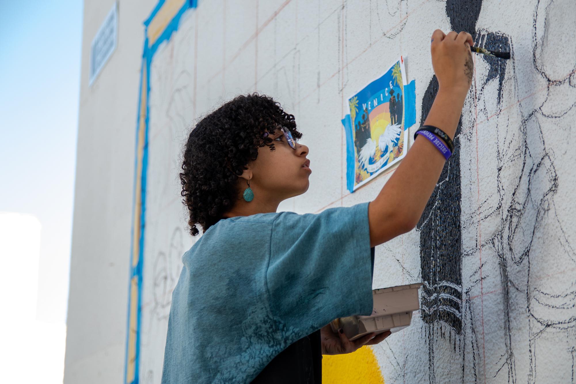 Vision of the future: Senior Jeannie Fischer helps paint a new mural between the West and Main Buildings during the final days before graduation. The mural is a collaboration between Venice's M.E.Ch.A chapter and Art Factory, a club dedicated to art-making. The mural centers on silhouettes with traditional Latin American clothing and a backdrop of a sunset on Venice Beach---adorned with palm trees, cempasúchil (also known as marigolds), and monarch butterflies.